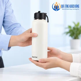 Bàn tay minh họa trao và nhận bình Rạng Đông trắng kem tại bàn tiếp khách.