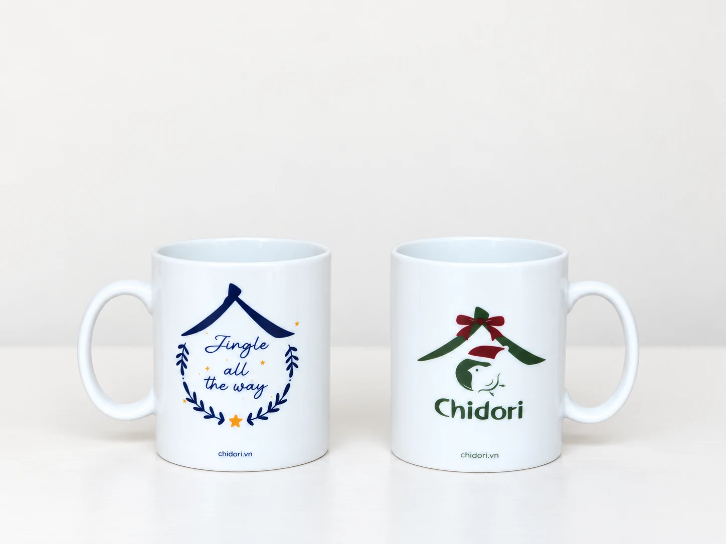 Hai cốc sứ trắng có quai, một cốc in thông điệp xanh và một cốc in logo Chidori.
