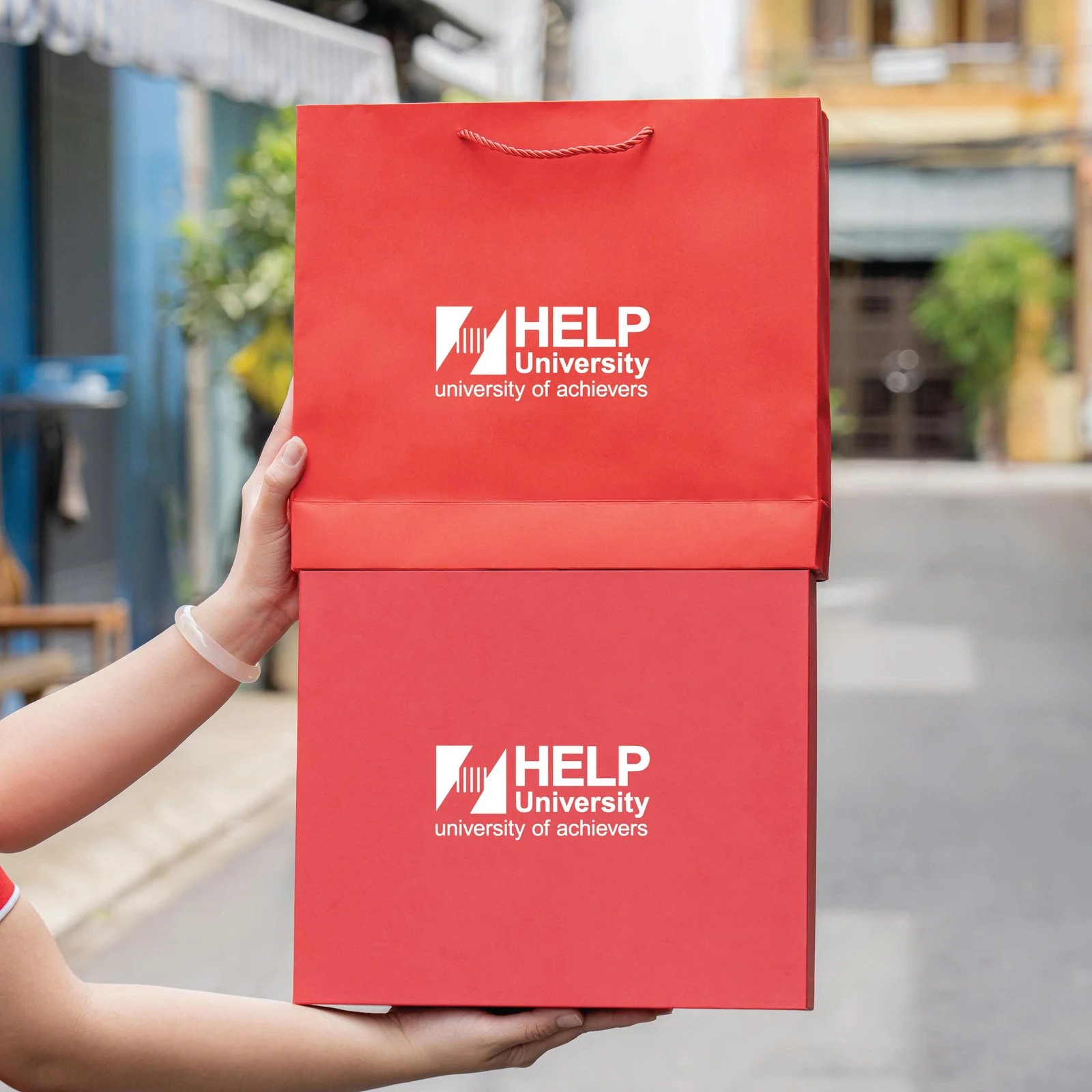 Ảnh thật hộp đóng và túi đỏ có nhận diện HELP University, chỉ thấy mặt ngoài.