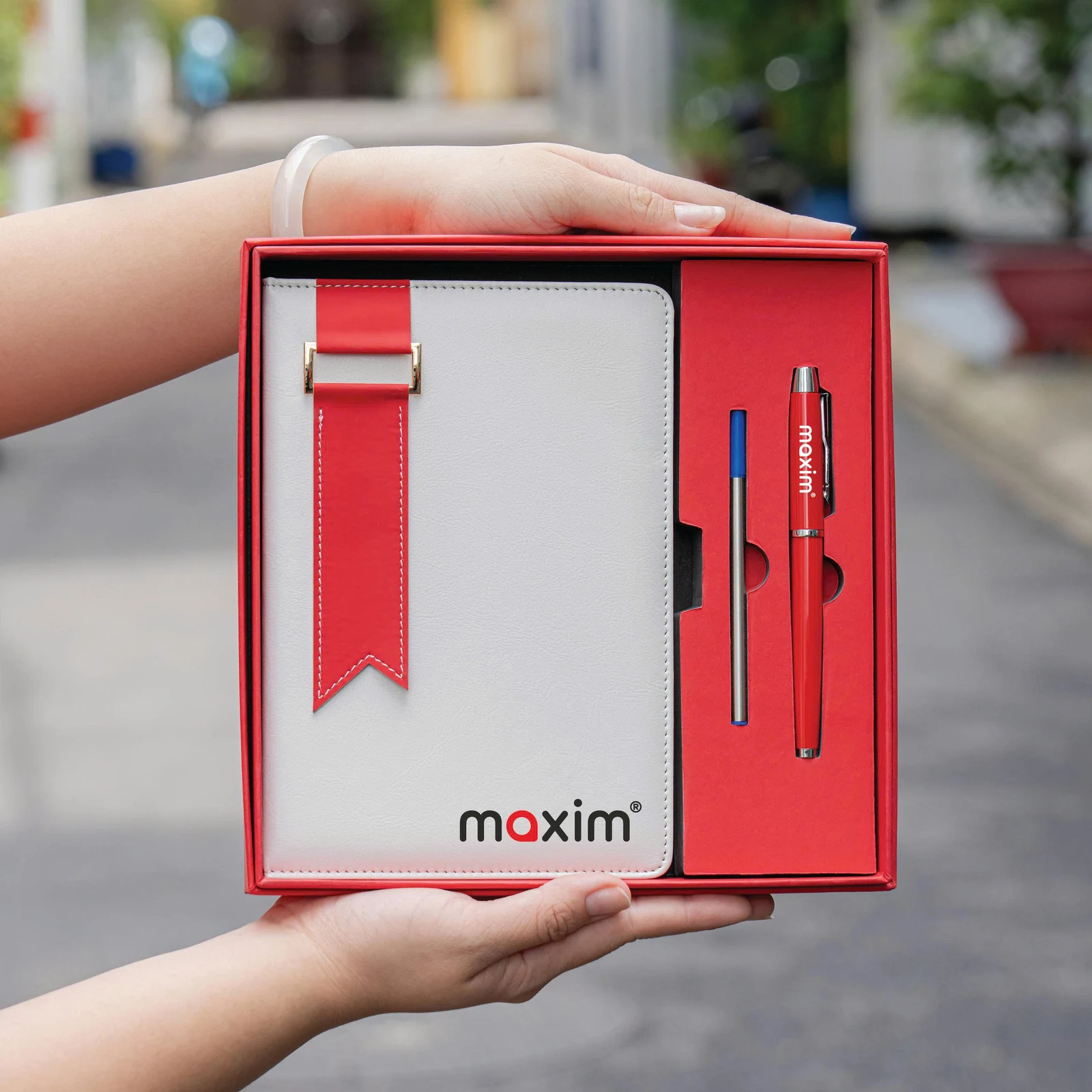 Ảnh thật sổ maxim trắng dải đỏ, bút và ruột thay trong khay đỏ.