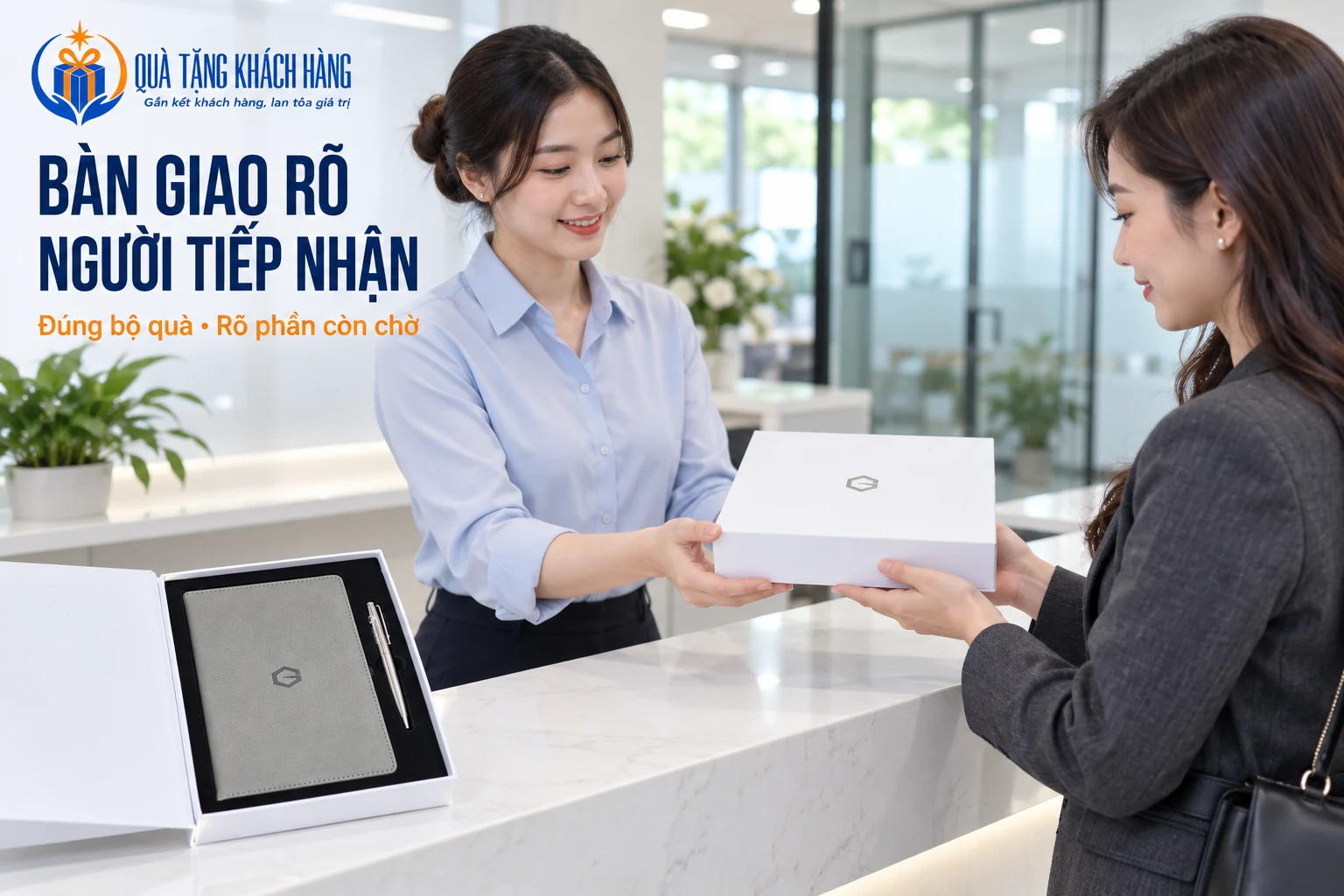 Hai người trao nhận hộp quà trắng tại quầy, bên cạnh mẫu sổ xám và bút bạc