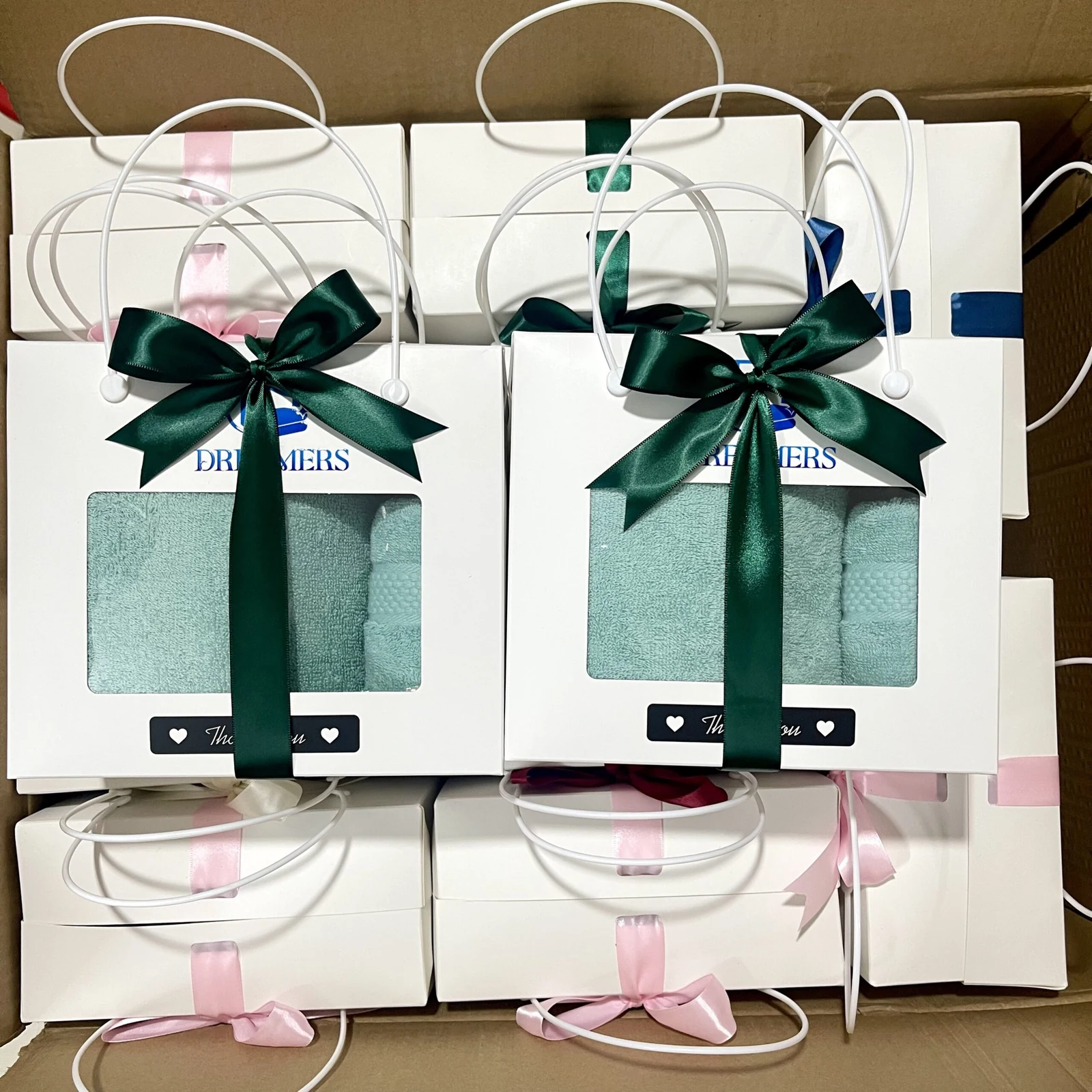 Các gói quà có quai, cửa sổ thấy khăn màu xanh và nơ xanh đậm đặt trong thùng carton.