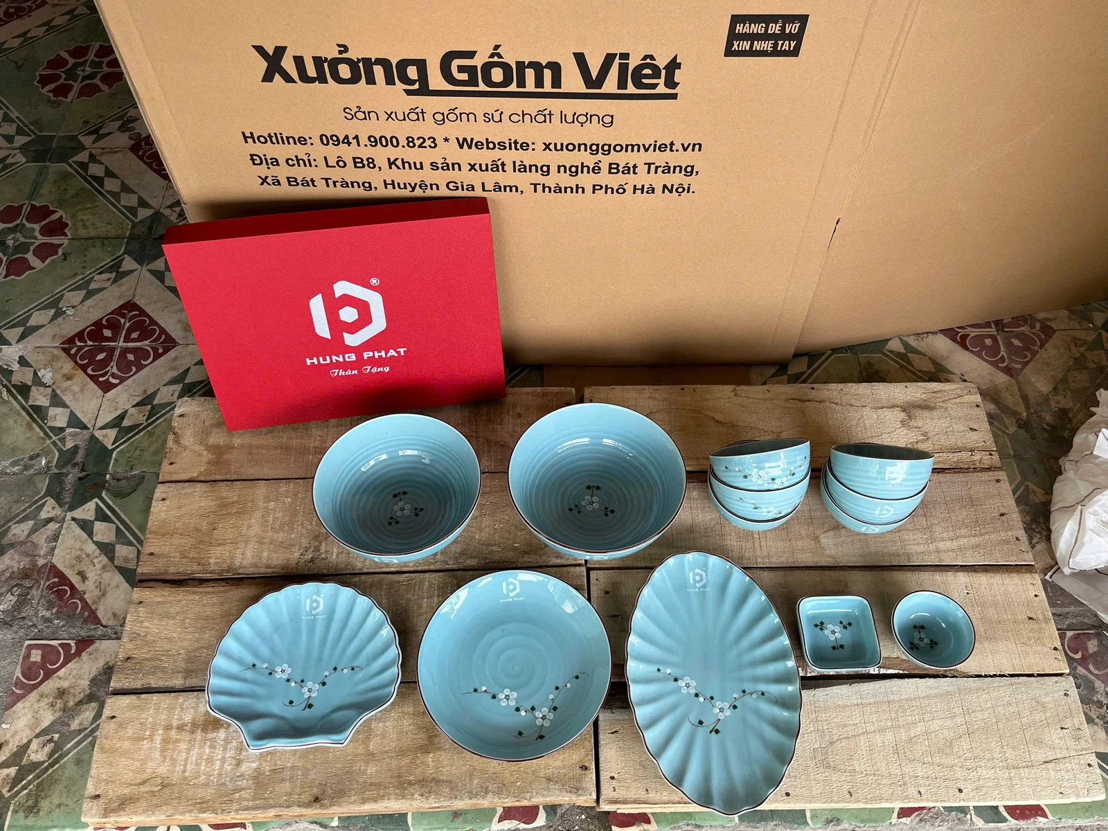 Bát, đĩa tròn, đĩa dáng lá và chén nhỏ màu xanh, có logo trên một số món.