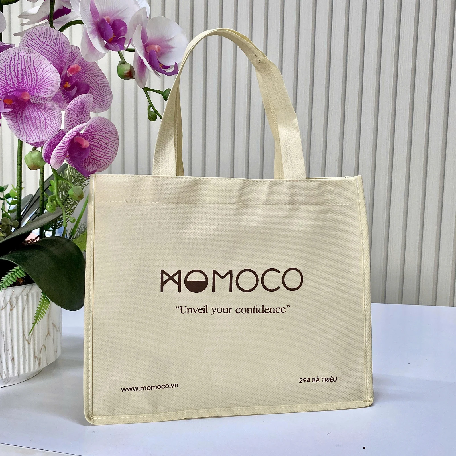 Ảnh thật túi sáng màu với logo Momoco, dòng chữ và thông tin ở các vùng mặt trước.