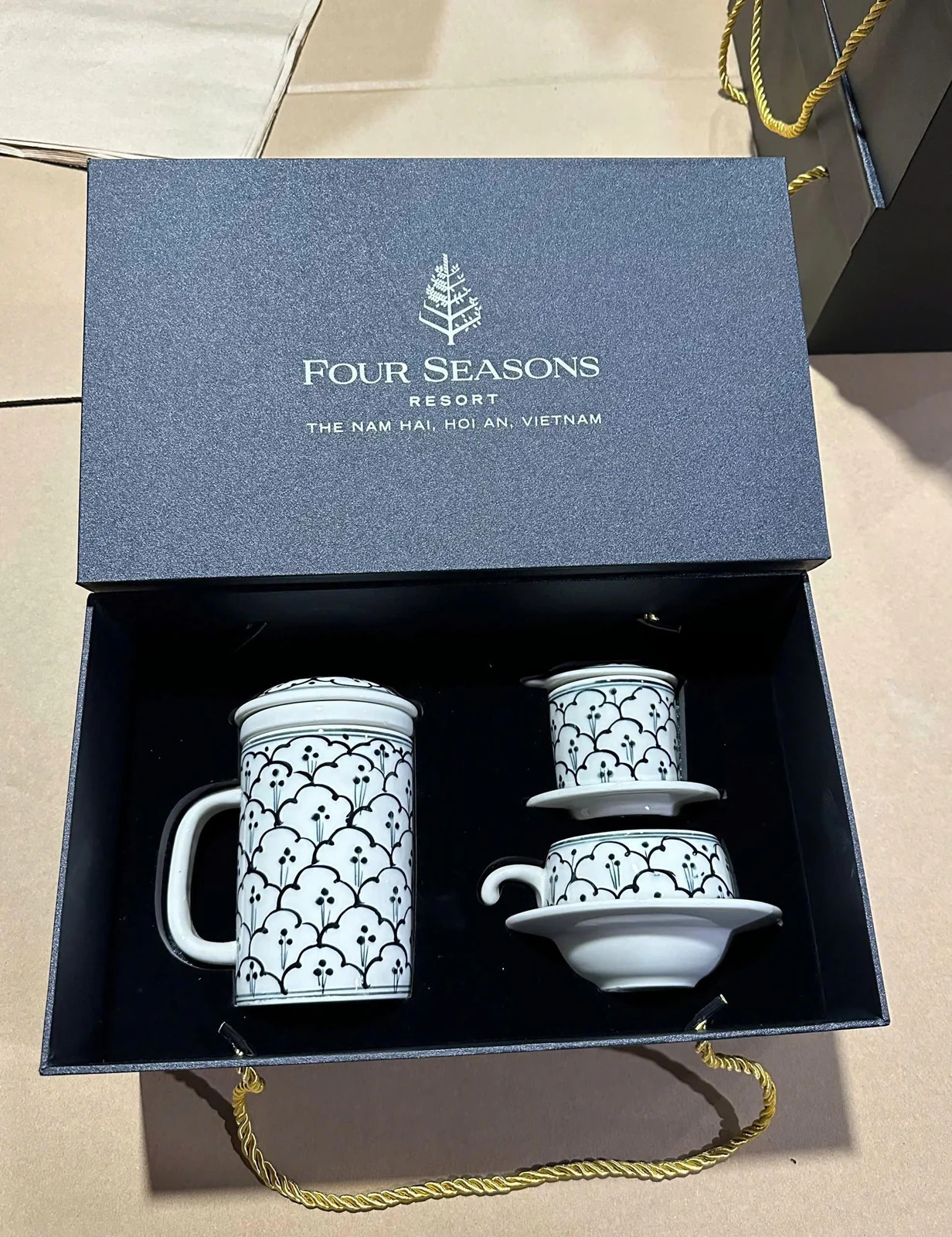 Bộ gốm trắng hoa văn đen đặt trong hộp nhận diện Four Seasons ở ảnh thật.