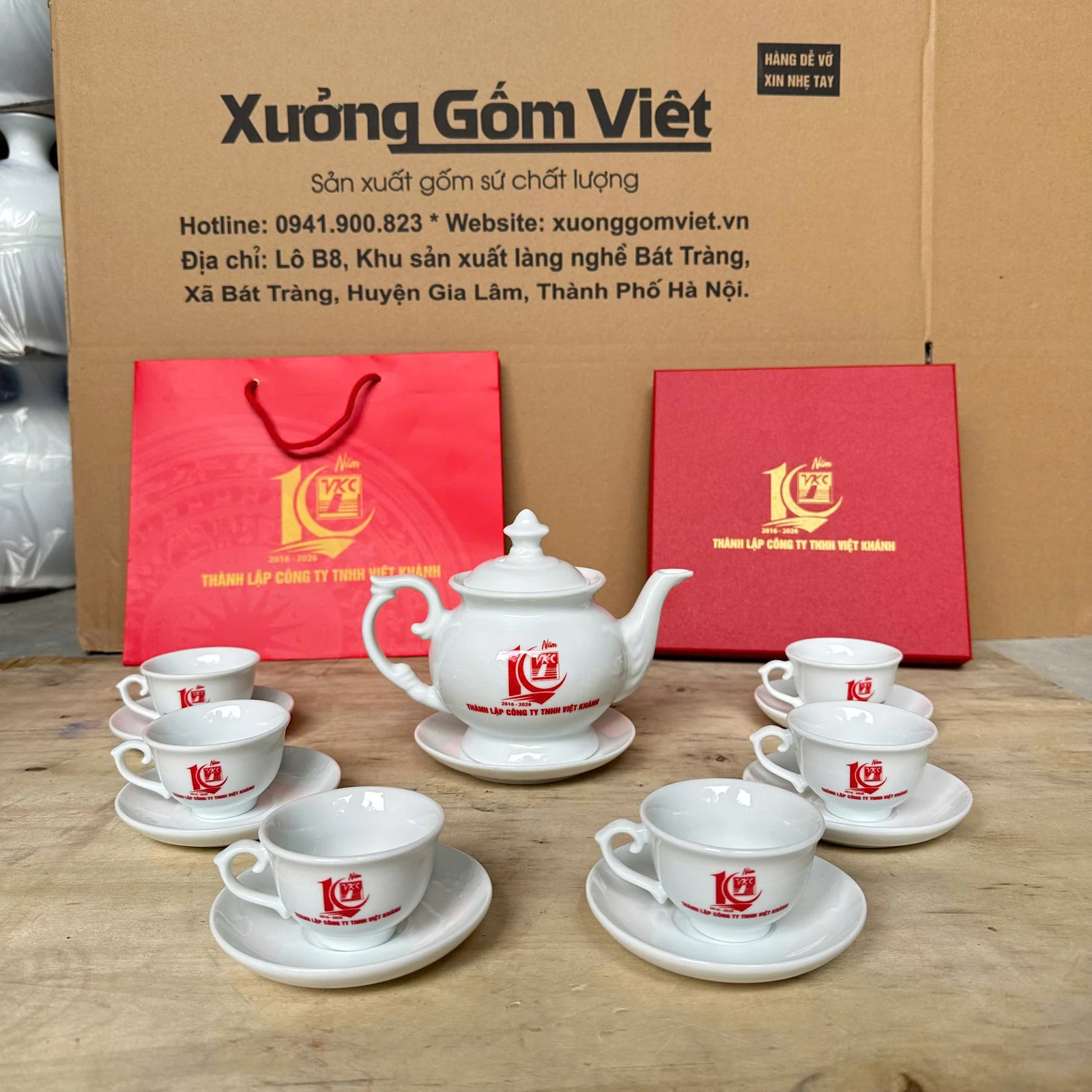 Bộ trà trắng có sáu tách, đĩa lót và nhận diện đỏ trong ảnh nguồn.