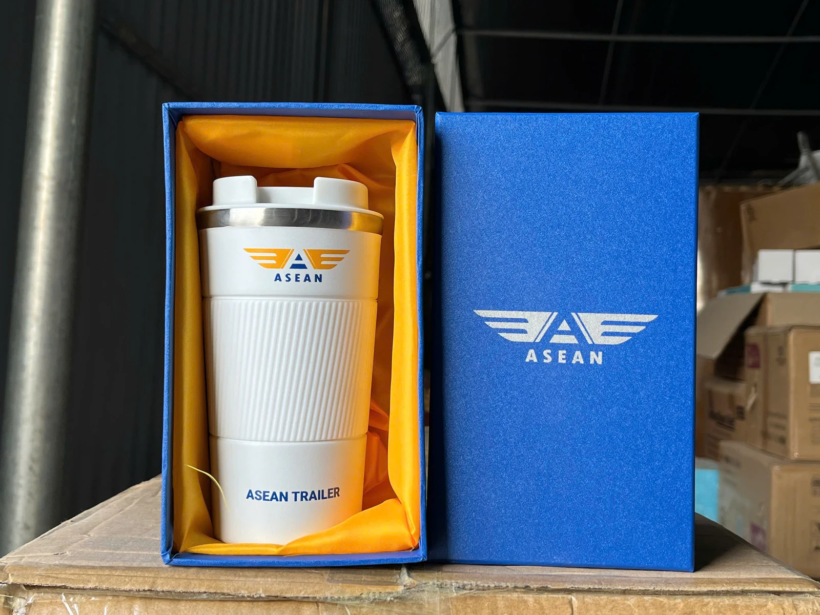 Cốc trắng thân có gân, nắp trắng và viền kim loại, đặt trong hộp xanh in nhận diện ASEAN.