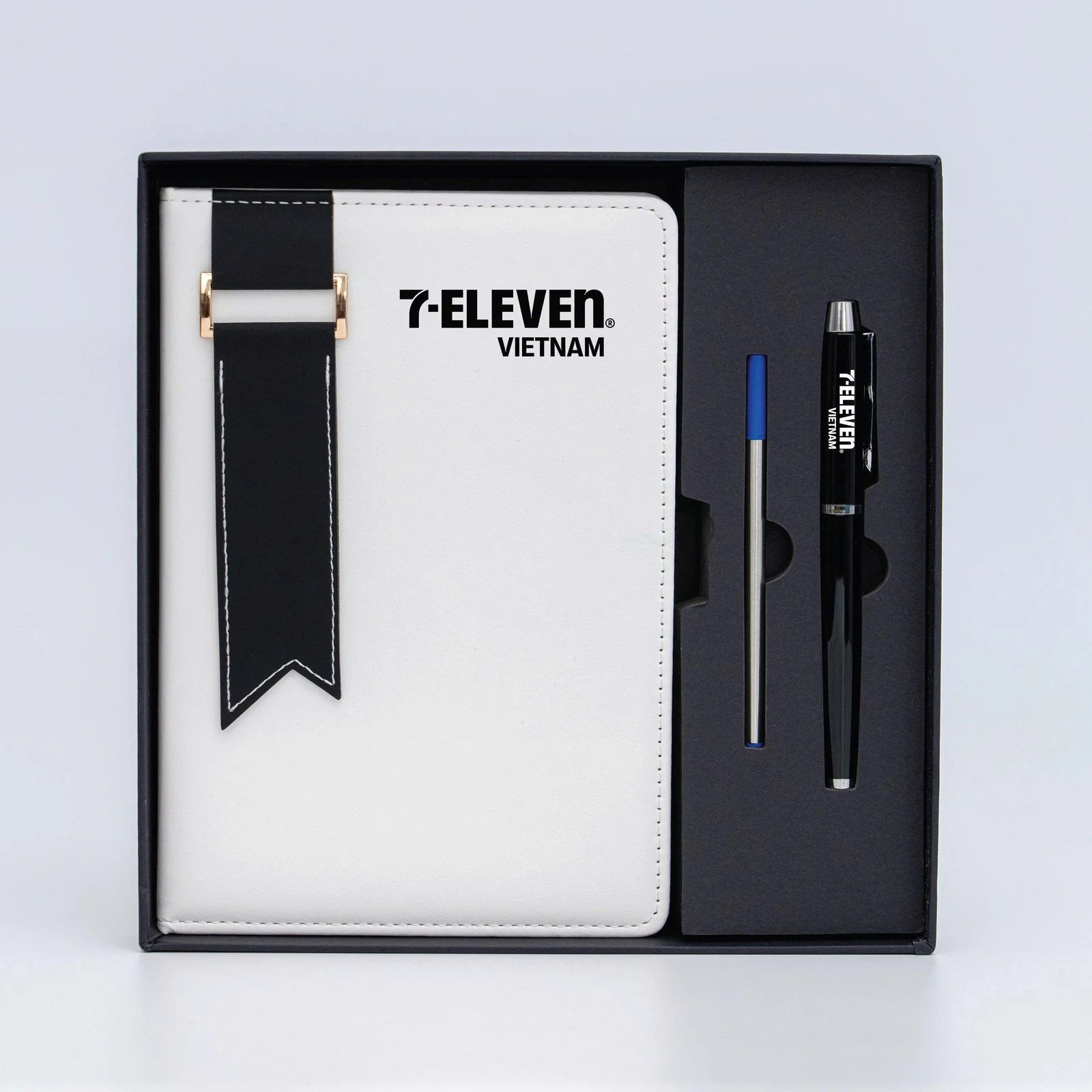 Sổ trắng dây đen và bút có nhận diện 7-Eleven trong hộp.