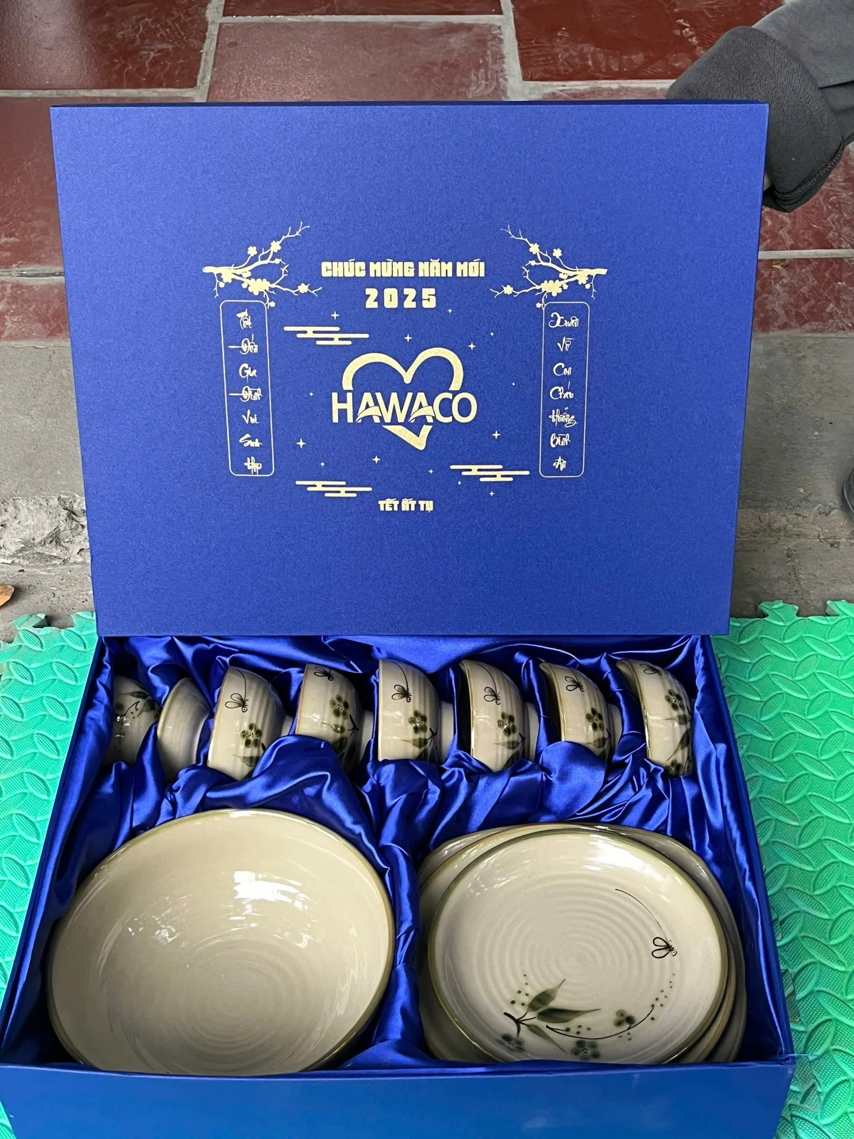 Hộp xanh mở nắp có nhận diện vàng, các bát và đĩa được bố trí trong lớp lót.