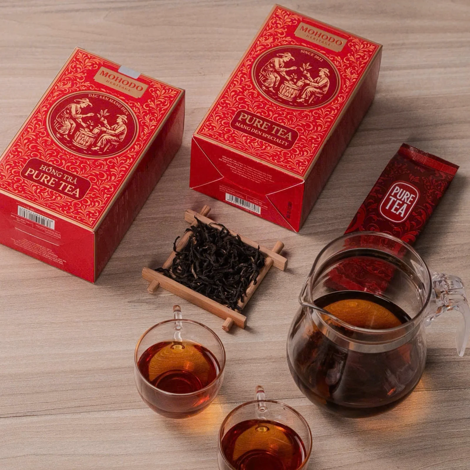 Ảnh nguồn các hộp và gói Pure Tea, lá trà trên khay cạnh bình pha.
