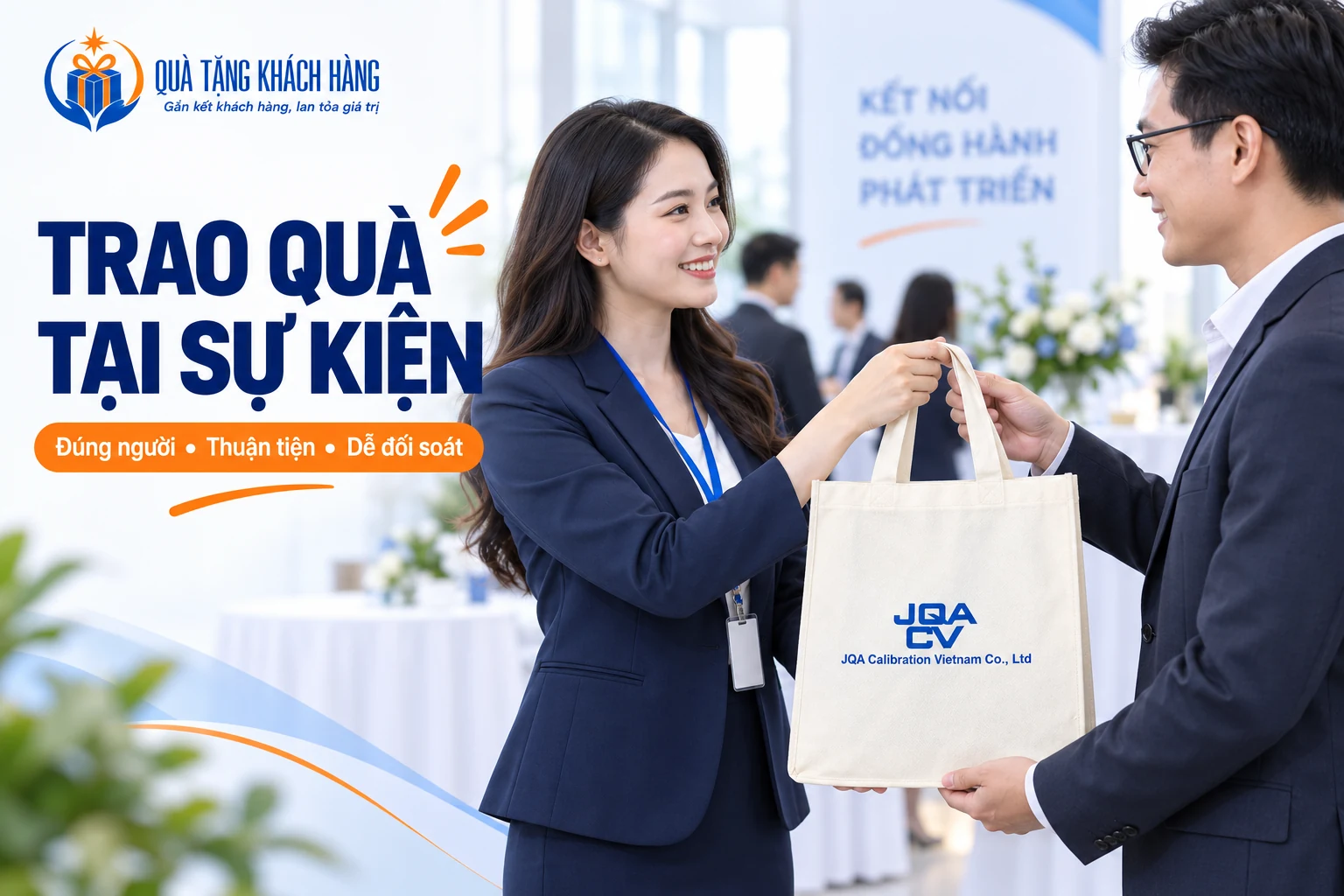 Hai người trao nhận túi màu kem in JQA trong không gian sự kiện sáng.