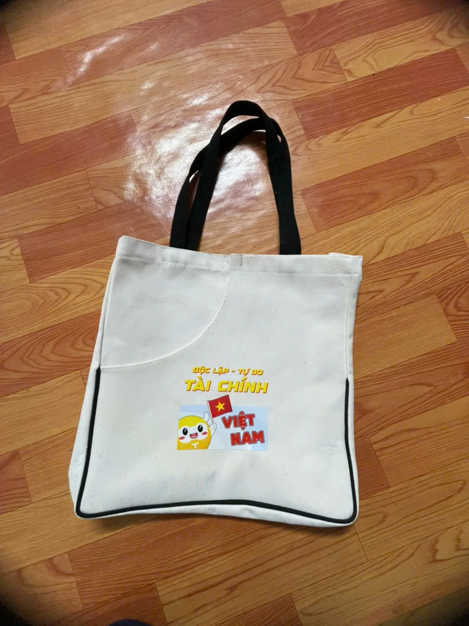 Túi trắng quai đen có hình in màu và viền đen trong ảnh gốc.