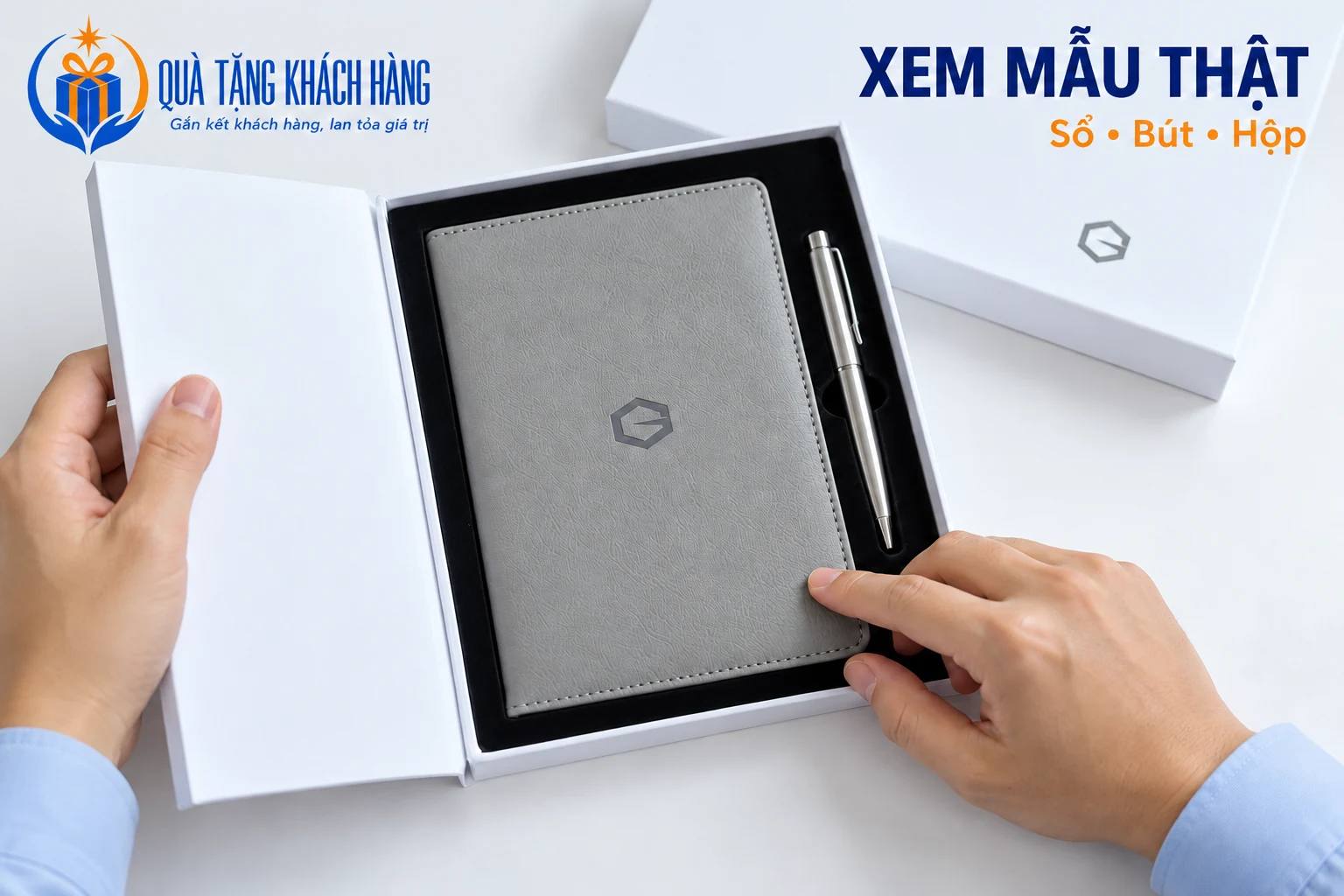 Cận tay xem bề mặt sổ xám, bút bạc và hộp trắng trong cảnh dựng